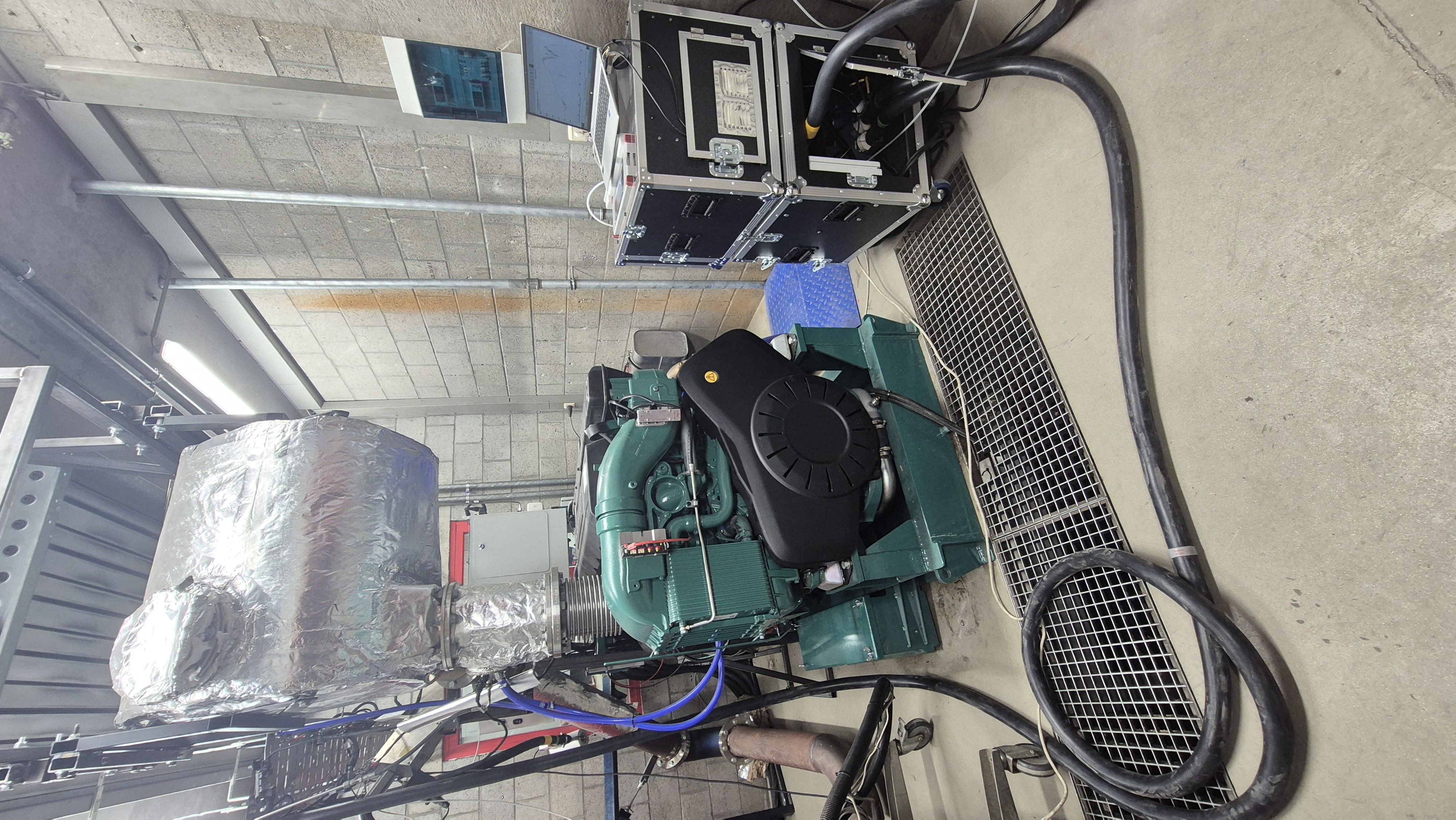 Volvo Penta-motor in de testcel met aangesloten leidingen, meetapparatuur en laptop.